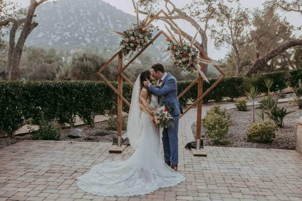 A bride and groom share a kiss beneath a rustic wooden arch